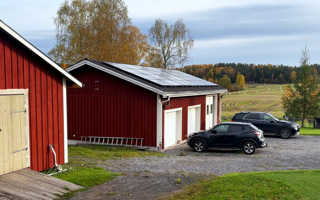 Rött garage med 80 solceller på taket, beläget på landsbygden med åkrar i bakgrunden.