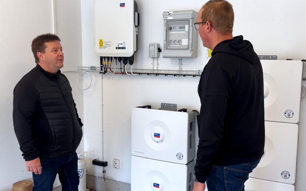 Två personer står framför ett batterisystem med fem SMA Home Storage-enheter på 16,4 kWh med smart styrning och backupfunktion.
