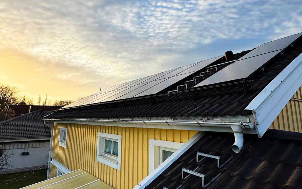 Solcellspaneler installerade på taket till en gul villa i solnedgång, som visar en modern energilösning för hushåll