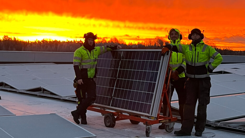 Montörer på Nordic Solar arbetar med installation av solpaneler på Solar Sveriges logistikcentrum under en dramatisk solnedgång.